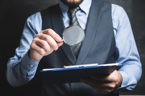 um-homem-de-terno-olha-documentos-com-uma-lupa-em-um-fundo-cinza_438099-2243